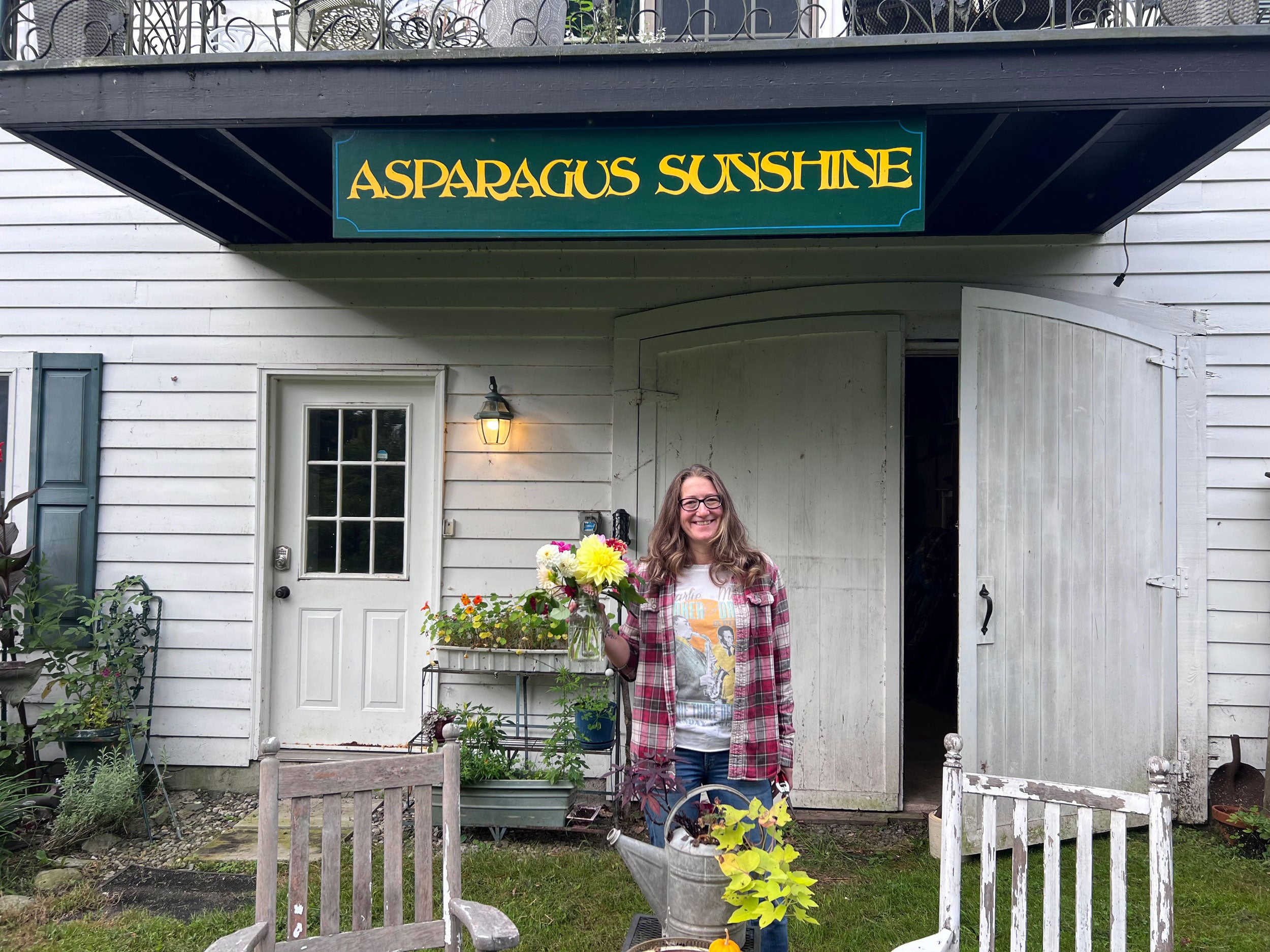 lauren chamberlain owner of asparagus sunshine holding flowers in front of a building with 'Asparagus Sunshine' sign
