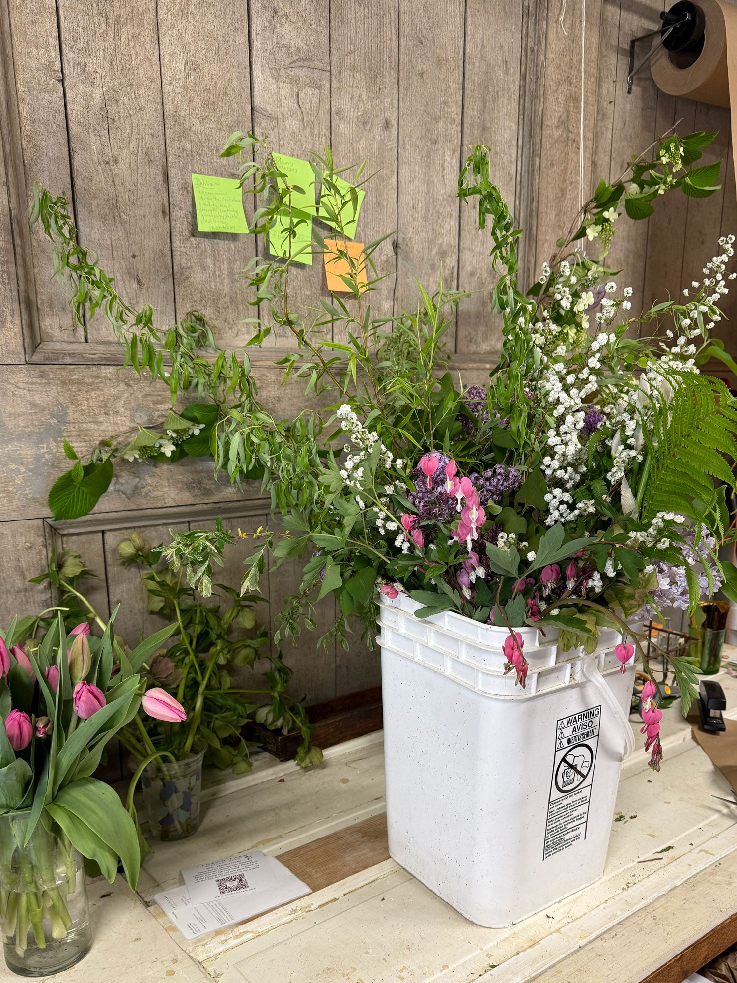 White bucket filled with flowers and plants against a wooden wall.