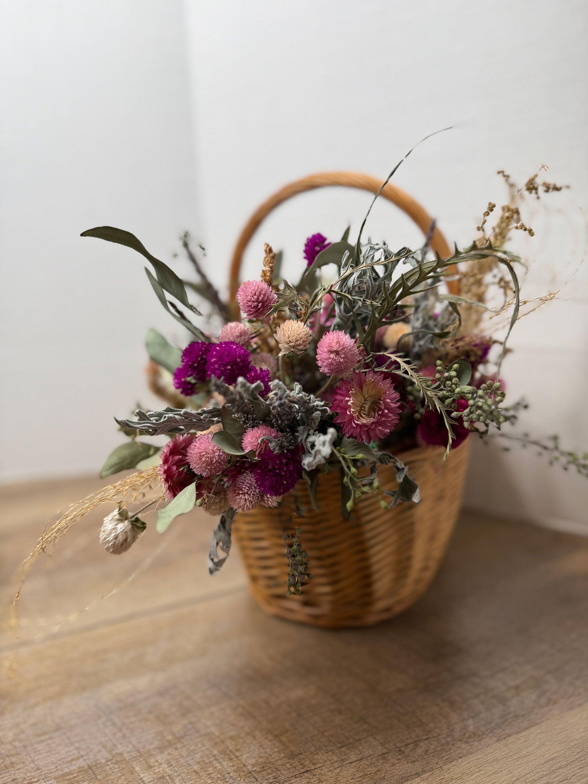 Wicker basket filled with a bouquet of dried flowers on a wooden surface