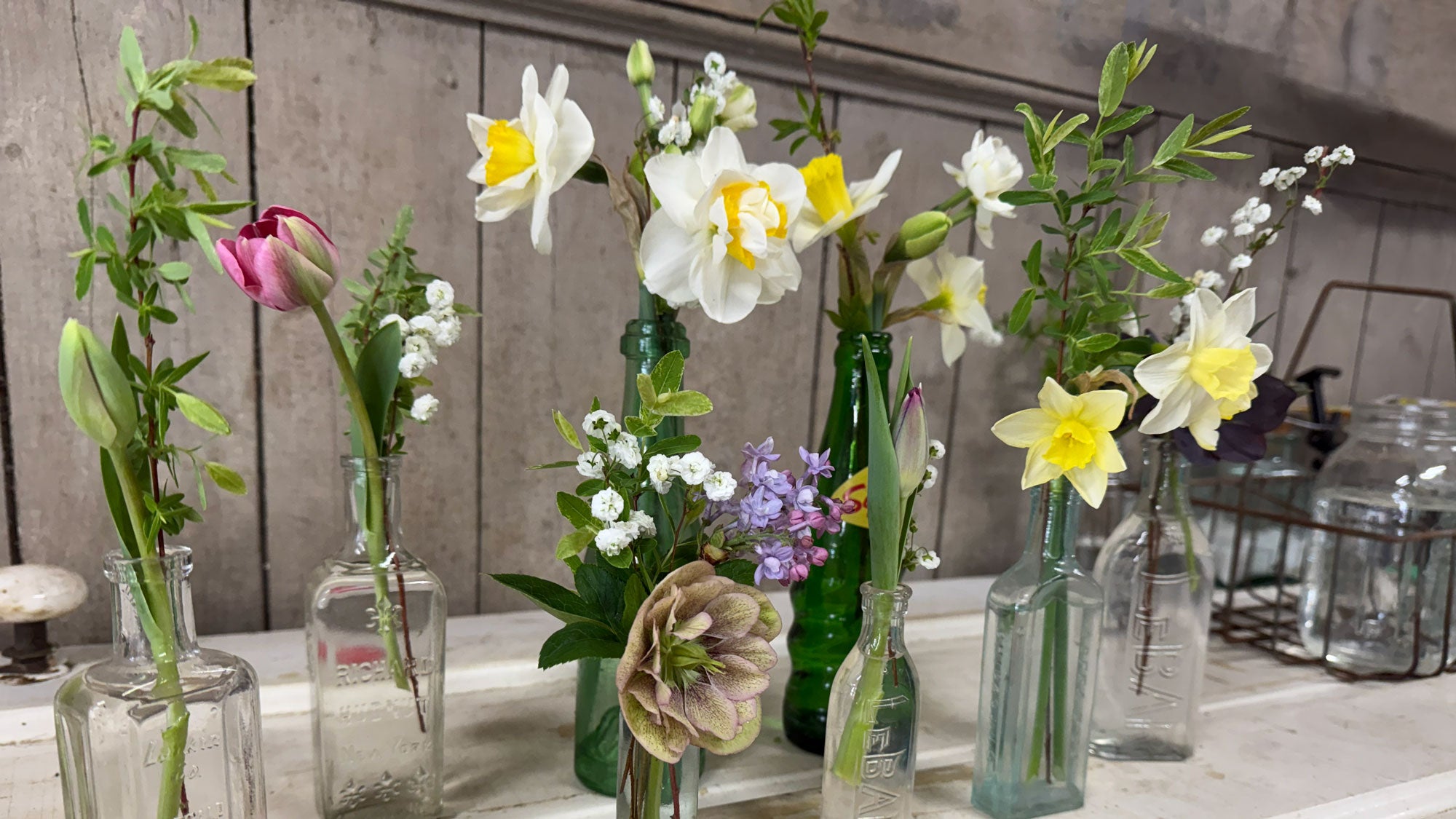 Various flowers in glass vases on a table with a concrete wall background