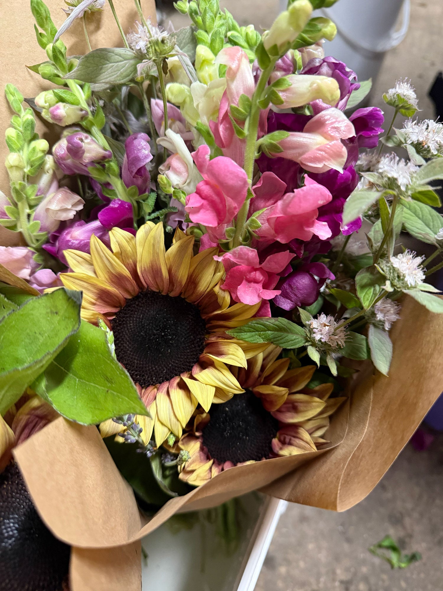 Bouquet of flowers with sunflowers and various other colors wrapped in brown paper.