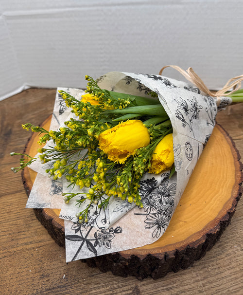 Bouquet of yellow flowers wrapped in decorative paper on a wooden surface