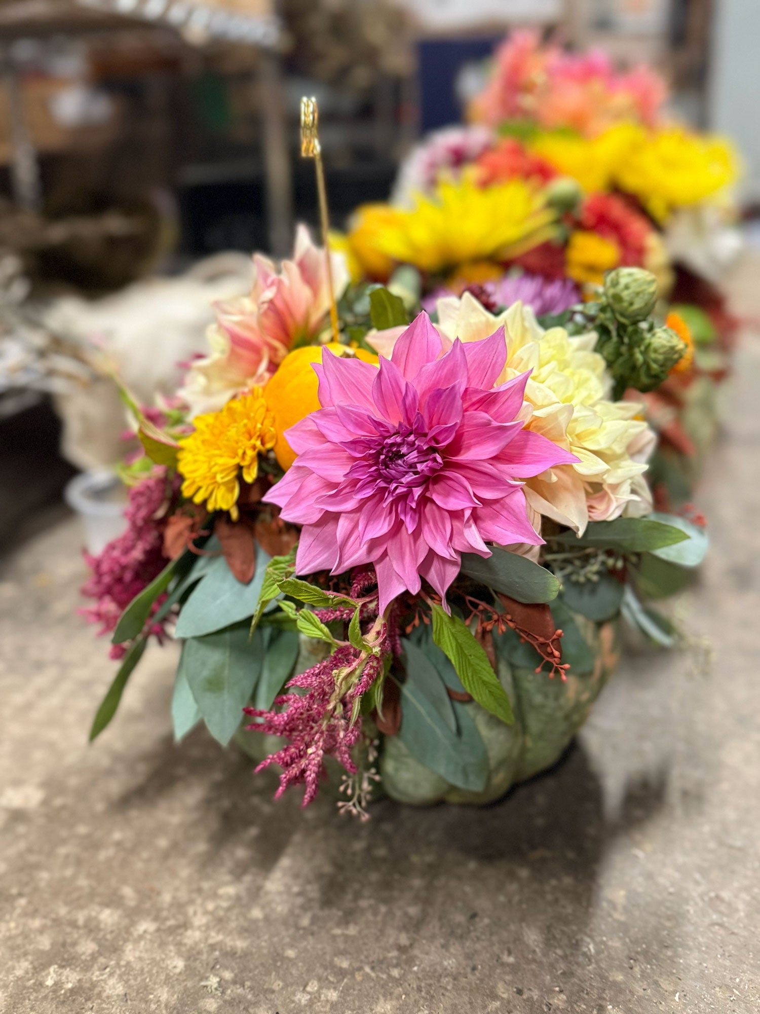Colorful flower arrangement in a pumpkin container on a concrete surface.