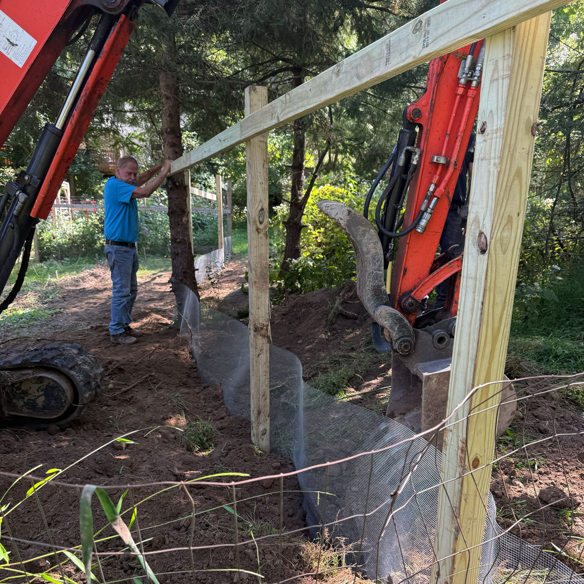 Person working with a construction vehicle near wooden posts outdoors