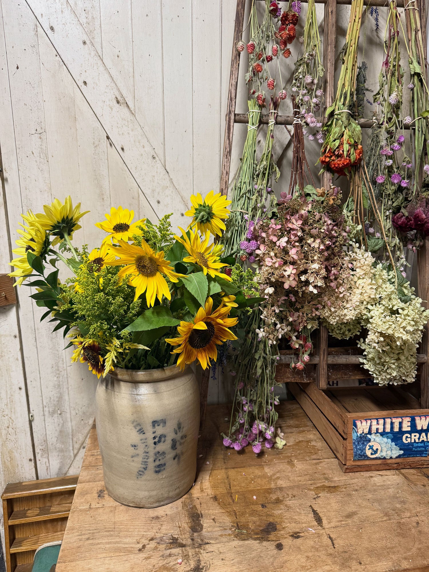 Decorative arrangement of sunflowers and dried flowers in a rustic setting with wooden crates.
