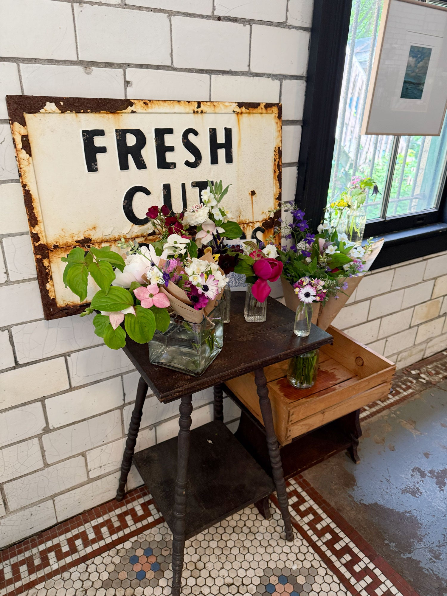 Vintage-style 'Fresh Cut' sign with flowers on a wooden table against a tiled wall.