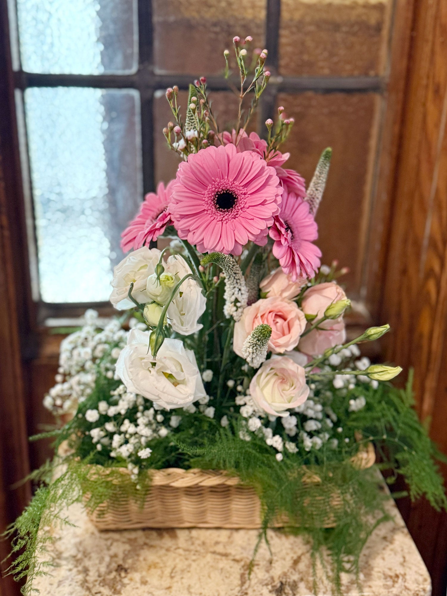 Floral arrangement with pink, white, and peach flowers in a woven basket on a stone surface.
